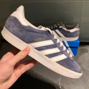 Blå Adidas Gazelle - Mörkblå adidas gazzel. Väldigt bra skick på mockan, sulan är vit men undersidan har varit bättre. Kommer med allt ”og”. Nypris 1200 vårat 500 men inte hugget i sten. Svarar på alla frågor. 
