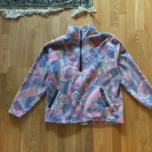 Färgglad fleece från F.lli Campagnolo - Säljer en färgglad fleece från F.lli Campagnolo med ett abstrakt mönster i rosa, grått och gult. Tröjan har en halv dragkedja och två fickor framtill. Perfekt för kyliga dagar!