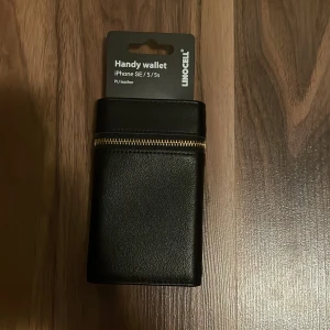 Svart plånboksfodral till iPhone 5/5s  - Säljer ett helt oanvänt plånboksfodral til iPhone 5/5s. Det är svart med guldfärgad dragkedja på utsidan och två fack för kort på insidan. 