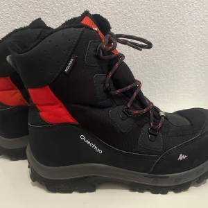 Svarta och röda vinterkängor från Quechua storlek 38 - Säljer ett par robusta vinterkängor från Quechua i svart och rött, storlek 38. Kängorna har snörning och är designade för att klara kalla och snöiga förhållanden. Perfekta för vinteräventyr och utomhusaktiviteter.