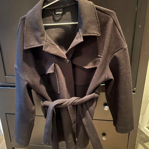 Svart kappa från Gina✨🖤 - Säljer min gammla kappa från Gina med ett band runt midjan, inga skador och väldigt fin skick! Perfekt nu till hösten, säljer för 200+frakt✨