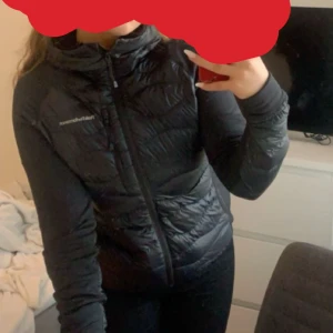 Peak Performance W Helium Down Hybrid - Svart - Svart hybridjacka från Peak Performance. Paneler i dun på jackans framsida, ryggen och ärmarna. Stängs framtill med dragkedja. Bröstficka som stängs med dragkedja, två fickor i sidan. Broderad logotyp på vänster ärm och bröst.