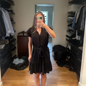 Svart klänning med volangdetaljer - Säljer en elegant svart klänning med volangdetaljer. Klänningen har en knytning i midjan vilket gör den väldigt justerbar. funkar både på vintern och sommaren.