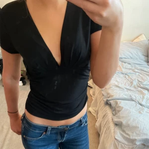 Svart v-ringad topp - Säljer en snygg svart topp med v-ringning. Den är kortärmad och har en tight passform som framhäver figuren. Perfekt för både vardag och fest!
