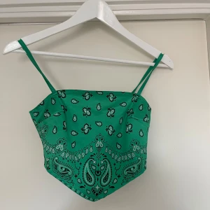 Grön bandana-mönstrad linnetopp - Snygg grön linnetopp med bandana-mönster. Toppen har smala axelband och en knytning i ryggen som ger en cool look. Perfekt för sommardagar eller festivaler!