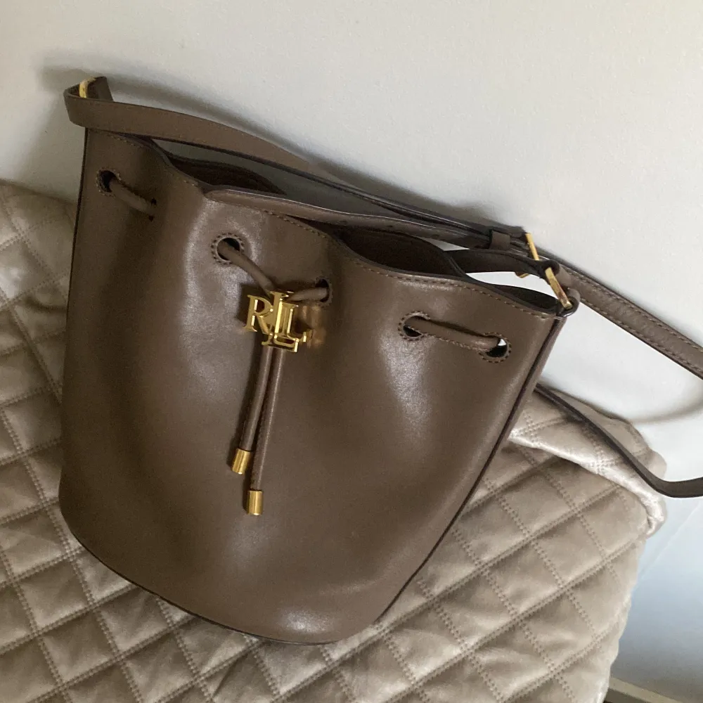 Ralph lauren väska, modell: Lauren Ralph Lauren Väska Andie 19 Drawstring  Nypris 4000kr Använd men i fint skick! Mått: B 24 x H 21 x D 13 cm Äkta läder!. Väskor.