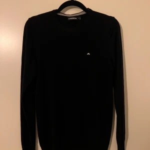 Svart tröja från J.Lindeberg - Snygg svart tröja från J.Lindeberg med diskret logga på bröstet. Tröjan har långa ärmar och en klassisk passform. Perfekt för en stilren look.