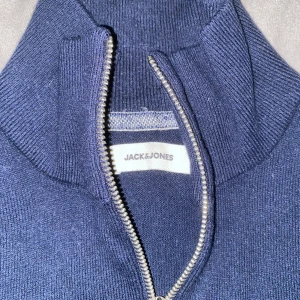 Mörkblå tröja med dragkedja från Jack & Jones - Säljer en stilren mörkblå tröja från Jack & Jones med dragkedja vid halsen. Perfekt för en avslappnad look. Tröjan har långa ärmar och är tillverkad i ett mjukt material.