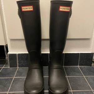 Svarta stövlar från Hunter - Säljer ett par klassiska svarta stövlar från Hunter. De är höga med justerbart spänne på sidan. Perfekta för regniga dagar och håller fötterna torra och bekväma.