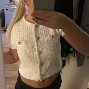 Vit ribbad kofta med guldknappar - Säljer en stilren vit ribbad kofta med korta ärmar och eleganta guldknappar. Koftan är croppad. super fin men kommer inte till användning! aldrig använd.