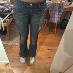 Blå bootcut jeans - Snygga blå bootcut jeans med slitningar och en klassisk femficksdesign. De har en låg midja och en bekväm passform som ger en avslappnad look. Perfekta för en casual stil.