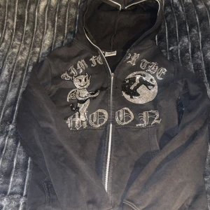 Aim  for the moon hoodie - Säljer en svart hoodie med dragkedja och coolt tryck på framsidan. Hoodien har en luva och texten 'Aim for the Moon' i glittriga bokstäver. Perfekt för en avslappnad stil.