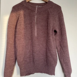 Rosa stickad tröja från NA-KD - Mysig rosa stickad tröja från NA-KD med en praktisk dragkedja framtill. Perfekt för kyligare dagar med sin varma och bekväma design. Tröjan har långa ärmar och en rund halsringning.