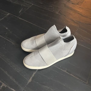 Grå stickade sneakers, Steve Madden - Snygga grå sneakers med stickad ovandel och elastisk passform. Skorna har en modern design med en bred elastisk rem över foten och en bekväm sula. de är i gott skick i Stl 42,5