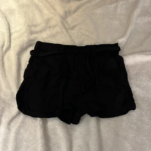 Svarta shorts med tyg bälte - Snygga svarta shorts med ett matchande tyg bälte. Använt fåtal gånger. Storlek 140. Tvättas och stryks innan den blir skickad. 