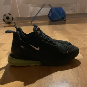 Svarta Nike sneakers med limegrön sula - Snygga svarta Nike sneakers med en iögonfallande limegrön sula. Skorna har en sportig design med snörning och en liten Nike-logga på sidan. Perfekta för en aktiv livsstil och ger en cool touch till din outfit.