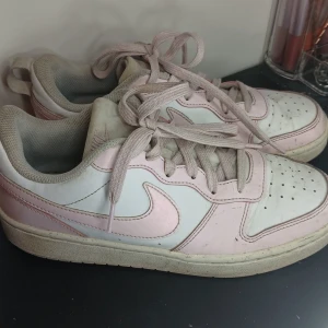 Nike cours i rosa och vitt - Säljer ett par Nike sneakers i en snygg kombination av rosa och vitt. Skorna har klassisk snörning och en bekväm passform. Perfekta för en avslappnad stil.