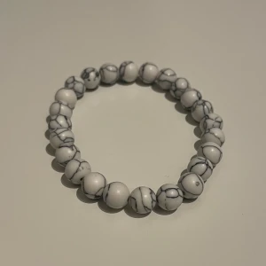 Vitt armband med marmorerade pärlor - Snyggt armband med vita marmorerade pärlor. Mycket bra kvalite och stretchig material. 