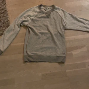 Grå tröja från Guess - Säljer en stilren grå tröja från Guess med rund hals och långa ärmar. Tröjan har en diskret logga på framsidan och är tillverkad i ett mjukt material. Perfekt för en avslappnad look.
