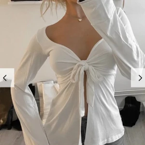 Vit långärmad topp med knyt - Snygg vit långärmad topp med knyt framtill som ger en trendig look. Toppen har en djup v-ringning och är perfekt för både vardag och festliga tillfällen. Passar bra till jeans eller kjol för en stilren outfit.