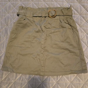 Beige kjol från Amisu - Snygg kjol från Amisu med ett bälte och dekorativ ring i midjan. Kjolen har en kort längd och praktiska fickor framtill. Perfekt för en stilren look.