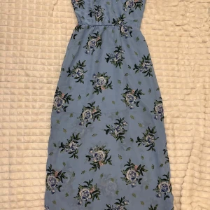 Blommig blå klänning - Söt blå klänning med blommigt mönster i grönt och rosa. Perfekt för sommarens varma dagar. Klänningen har en smickrande passform och ärmlös design.