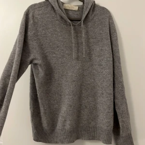 Kaschmir hoodie  - Säljer en mjuk och bekväm grå hoodie i kashmir från Sayless. Tröjan har en klassisk design med huva och ribbade muddar vid ärmslut och nederkant. Perfekt för kyliga dagar och passar till allt. Tyvärr så har tröjan fått två hål ett på armen och ett under armen.