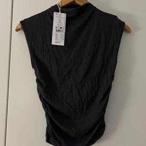 Svart ärmlös topp med hög krage - Snygg svart ärmlös topp från Arket med hög krage. Perfekt för en stilren look. Materialet är mjukt och bekvämt.