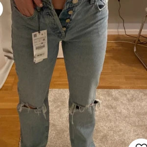 Blå jeans med hål från Zara - Snygga blå jeans från Zara med trendiga slitningar på benen. Perfekta för en avslappnad stil. Aldrig använda, lappar och allt finns kvar. Skriv för mer bilder eller mått. 🩵🩵 (Dessa byxor säljs inte längre) Orginalpris: ca 600/700 kronor. (De 2 första bilderna är lånade)