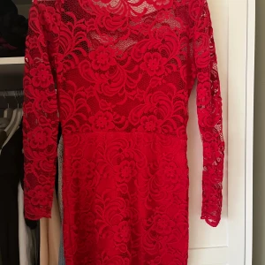 Röd spetsklänning - Snygg röd spetsklänning med blommigt mönster och långärmad design. Perfekt för en elegant kväll med sin vackra spetsdetalj och figurnära passform. Klänningen har en rund hals och är knälång, vilket ger en sofistikerad look.
