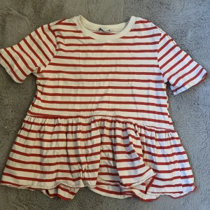 Randig topp från Zara - Säljer en söt randig topp från Zara i rött och vitt. Toppen har korta ärmar och en volangdetalj vid nederkanten som ger en lekfull touch. Perfekt för en avslappnad stil.endast använt 1 gång inga fläckar 👍😊