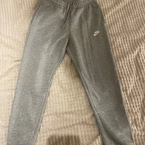 Grå mjukisbyxor från Nike - Säljer ett par grå mjukisbyxor från Nike med elastisk midja och snörning. Byxorna har en bakficka och ett broderat Nike-logotyp på framsidan. 