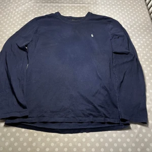Mörkblå långärmad tröja från Ralph Lauren - Säljer en stilren mörkblå långärmad tröja från Ralph Lauren med det klassiska broderade logotypen på bröstet. Perfekt för en avslappnad men ändå snygg look. Passar bra till jeans eller chinos.