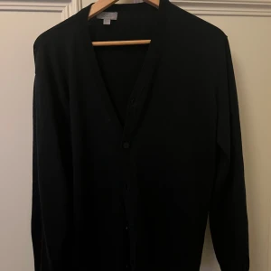 Svart kofta med knappar - Säljer en stilren svart kofta med knappar framtill. Perfekt för lager-på-lager och passar till många olika outfits. Koftan har långa ärmar och en klassisk design.