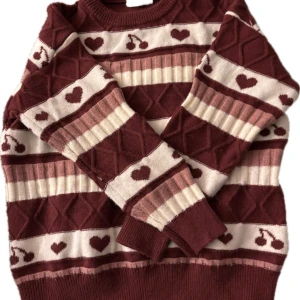 Vinröd tröja med hjärtmönster - Säljer en mysig oversized vinröd tröja med ett gulligt hjärtmönster. Tröjan har långa ärmar och ribbade muddar vid ärmslut och nederkant. Perfekt för kyliga dagar!