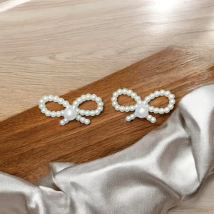 Örhängen med pärlor i rosettform - Eleganta örhängen formade som rosetter, dekorerade med vita pärlor. Perfekta för att ge en sofistikerad touch till din stil. De har en klassisk och tidlös design som passar många tillfällen.