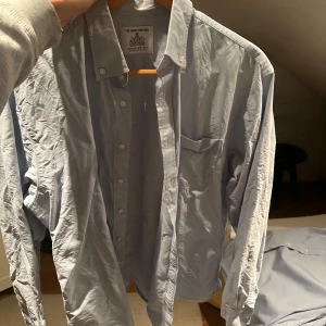 Ljusblå skjorta från The Shirt Factory - Snygg ljusblå skjorta från The Shirt Factory i regular fit. Skjortan har långa ärmar och en klassisk krage med knappar. Perfekt för en stilren look.