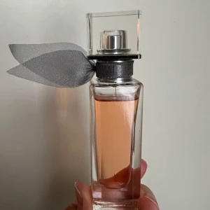 La Vie Est Belle Eau de Parfum från Lancôme - Bara sprayat några få gånger, 90% full. Upptäck La Vie Est Belle från Lancôme, en elegant parfym med en söt och fruktig doftprofil. Flaskan är stilrent designad med en rosa vätska och en silverfärgad rosett vid halsen. Perfekt för den som älskar en kombination av vanilj, patchouli och vita blommor.