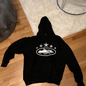 Svart hoodie med stjärnmotiv - Säljer en svart hoodie med ett coolt stjärnmotiv på bröstet. Perfekt för en avslappnad stil och bekväm att bära. Den har en klassisk passform med långa ärmar och en praktisk huva.