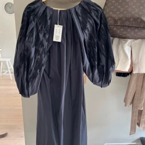 Svart långklänning med puffärmar från COS - Elegant svart långklänning med unika puffärmar och ett subtilt mönster. Perfekt för en stilfull kväll. Klänningen har en rund hals och en rak passform som ger en sofistikerad look. 34 i storlek men passar en storlek S. Nypris 990 kr