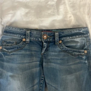 Blå jeans från My God! - Snygga ljusblå jeans från My God! med en klassisk femficksdesign och dekorativa sömmar på bakfickorna. De har en lågmidjad passform och är hyfsat utsvängda. Satt in ett snöre i midjan som ej märks när man har på sig jeansen. Säljer därför att de är för stora även köpt från vinted nyligen. Innerbenslängd-82 midjemått-43 rakt över 💓priset kan diskuteras 
