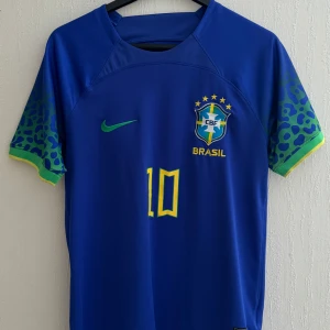 Blå Brasilien fotbollströja med Neymar Jr - Blå Brasilien borttröja med Neymar Jr och nummer 10 på ryggen. Tröjan är knappt använd och den säljs pga för liten för mig. Pris kan diskuteras. Perfekt till sommaren!