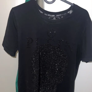 Svart t-shirt från Philipp Plein - Snygg svart t-shirt från Philipp Plein med glittrande dödskallemotiv på framsidan. T-shirten har korta ärmar och rund halsringning. Perfekt för dig som vill sticka ut med stil. 🖤✨
