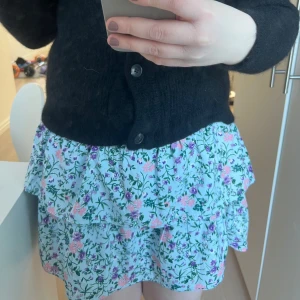 Blommig kjol från Vero Moda - blommig kjol från Vero Moda i ljusblått med volanger. Kjolen har ett elastiskt midjeband och ett färgglatt blommönster i rosa och lila nyanser. Perfekt för en somrig look!