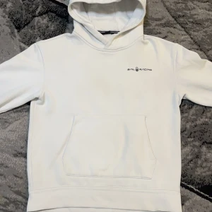 Vit hoodie från Sail Racing - Säljer en stilren vit hoodie från Sail Racing. Den har en klassisk design med en känguruficka framtill och en bekväm huva. Perfekt för en avslappnad look. Storlek 176 men passar Xs,S