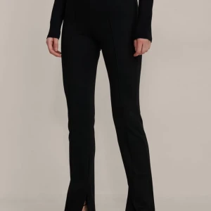 Svarta byxor med slits - Snygga svarta byxor med slits vid anklarna. De har en tight passform och är perfekta för en stilren look. Byxorna är högmidjade och gjorda i ett bekvämt material som ger en smickrande siluett.