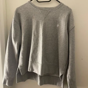 Grå sweatshirt från Polo Ralph Lauren - Säljer en stilren grå sweatshirt från Polo Ralph Lauren. Tröjan har långa ärmar och en liten slits på sidorna. Den är perfekt för en avslappnad look och har en diskret logga på bröstet. Passar bra till både jeans och joggers.