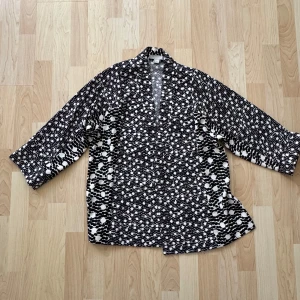 Svartvit mönstrad jacka - Säljer en unik svartvit mönstrad jacka/ kimono med trekvartsärm och tillhörande midjeskärp. Jackan har ett iögonfallande mönster och en lös passform som ger en avslappnad look. Perfekt för att lägga till lite stil till din outfit.