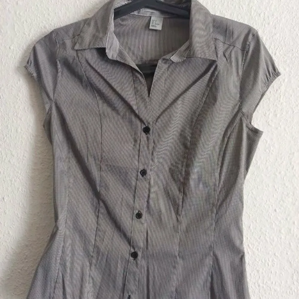 Snygg grå blus med korta ärmar och knappar framtill. Perfekt för en stilren look med en klassisk krage och figurnära passform.. Paidat.