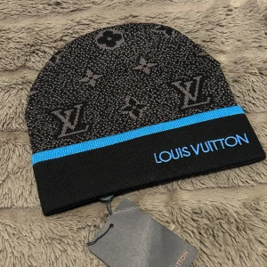 Svart mössa från Louis Vuitton - Snygg svart mössa från Louis Vuitton med ikoniskt mönster och en blå rand. Perfekt för att hålla stilen i kallare väder. Den har en broderad logotyp i blått som ger en exklusiv touch.. två styckna för 1500 en för 750